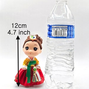 May include: A small doll wearing a traditional Korean hanbok dress. The doll is 4.7 inches tall and is standing next to a clear plastic water bottle for size comparison.