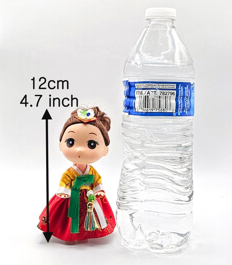 May include: A small doll wearing a traditional Korean hanbok dress. The doll is 4.7 inches tall and is standing next to a clear plastic water bottle for size comparison.