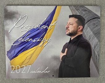 May include: A 2027 calendar featuring a portrait of President Zelenskyy with his hand over his heart. A large blue and yellow Ukrainian flag waves in the background against a cloudy sky. The text reads President Zelenskyy 2027 calendar.