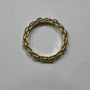 Puede incluir: Un anillo dorado con un dise&ntilde;o de eslabones de cadena. El anillo es circular y parece estar hecho de metal. El patr&oacute;n de eslabones de cadena se repite alrededor de toda la banda del anillo.