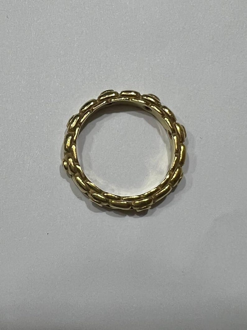 Puede incluir: Un anillo dorado con un dise&ntilde;o de eslabones de cadena. El anillo es circular y parece estar hecho de metal. El patr&oacute;n de eslabones de cadena se repite alrededor de toda la banda del anillo.