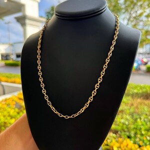 May include: A gold chain necklace with a mariner link design. The chain is displayed on a black mannequin bust.