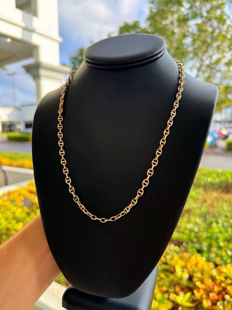 May include: A gold chain necklace with a mariner link design. The chain is displayed on a black mannequin bust.