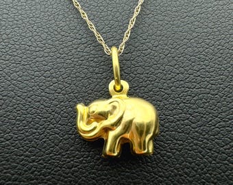 May include: A polished gold-tone elephant pendant suspended from a delicate gold-tone rope chain. The elephant charm is depicted in profile with its trunk curled upward, featuring a smooth, reflective surface and a small circular bail at the top.