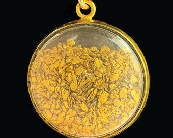 Peut inclure: Un pendentif rond de couleur or avec un couvercle transparent en forme de dôme. À l'intérieur, de nombreux petits flocons d'or irréguliers sont visibles. Le pendentif a une petite boucle en haut pour une chaîne. Le fond est noir.
