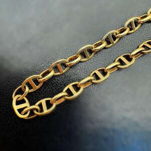 May include: A gold chain necklace with a mariner link design. The chain is made of thick, solid links.