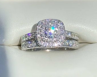 Peut inclure: Un ensemble de bagues de fiançailles en diamant avec un design de halo carré. La pierre centrale est entourée de petits diamants, et la bague comporte également des diamants. La bague est sertie dans un métal blanc, probablement du platine ou de l'or blanc.