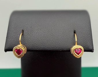 May include: A pair of gold drop earrings featuring heart-shaped red gemstones set in a gold frame. The earrings have a curved wire hook design that attaches to the top of each heart-shaped setting, showcasing a polished gold finish throughout.