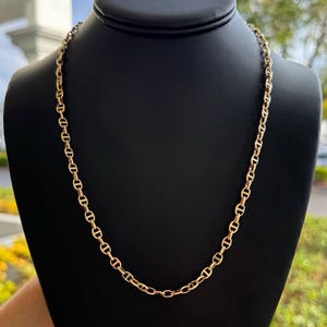 May include: A gold chain necklace with a mariner link design. The chain is on a black display stand.