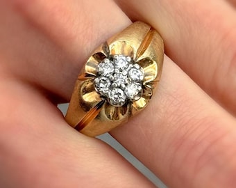 Peut inclure: Une bague en or ornée d'un groupe de petits diamants ronds disposés en forme de fleur. La bague a un large anneau avec une finition texturée et un détail de rainure subtil sur les côtés. Les diamants brillent sur l'or chaud.