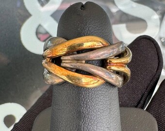 Peut inclure: Une bague multicolore avec des bandes entrelacées d'or, d'argent et de bronze. La bague est présentée sur un support noir, mettant en valeur son design complexe et ses teintes métalliques. La conception de la bague présente une série de boucles imbriquées.