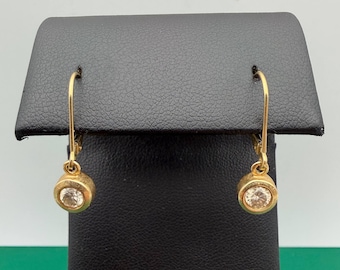 May include: A pair of gold drop earrings featuring a single round, clear gemstone set in a circular bezel. Each earring is suspended from a curved gold wire hook, providing a simple and classic design that hangs vertically from the top support.