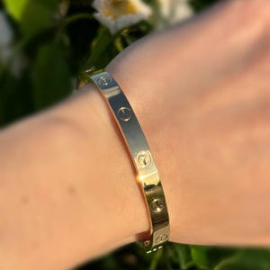 May include: A gold-tone bangle bracelet with a repeating screw design.