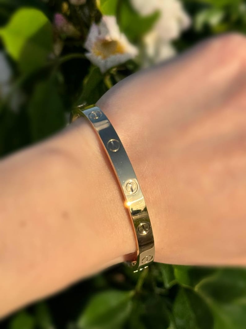 May include: A gold-tone bangle bracelet with a repeating screw design.