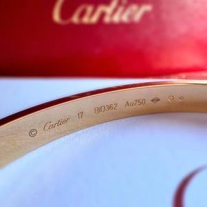 May include: A gold Cartier bracelet with the inscription 'Cartier 17 BID362 Au750' on the inside.