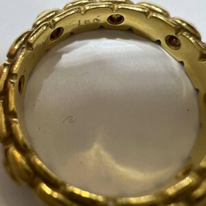 Puede incluir: Primer plano de un anillo de oro con un dise&ntilde;o repetitivo en forma de hoja. El anillo tiene peque&ntilde;as piedras redondas incrustadas. El interior del anillo es liso y reflectante. El anillo est&aacute; marcado con "18K".