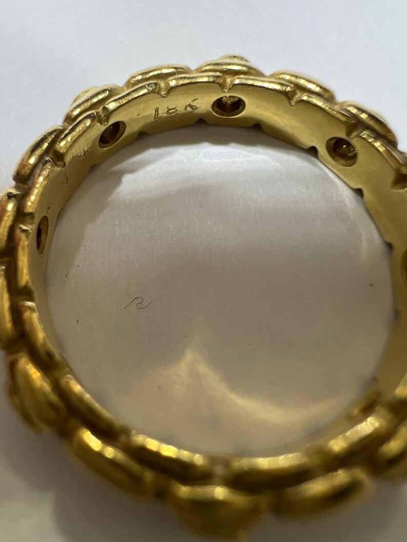 Puede incluir: Primer plano de un anillo de oro con un dise&ntilde;o repetitivo en forma de hoja. El anillo tiene peque&ntilde;as piedras redondas incrustadas. El interior del anillo es liso y reflectante. El anillo est&aacute; marcado con "18K".