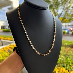 May include: A gold chain necklace with a mariner link design. The chain is displayed on a black mannequin bust.