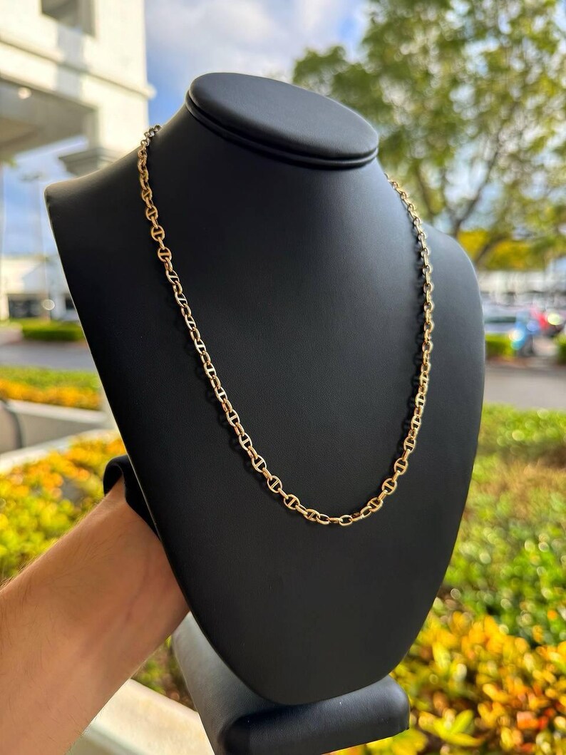 May include: A gold chain necklace with a mariner link design. The chain is displayed on a black mannequin bust.