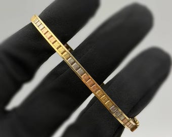 May include: A slim, hinged bangle bracelet featuring a repeating pattern of alternating yellow, rose, and white gold-toned segments. The metal surface displays a fine, brushed texture throughout, and the piece includes a secure clasp mechanism.