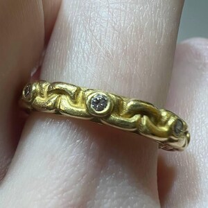 Puede incluir: Un anillo de oro con un dise&ntilde;o texturizado y tejido. El anillo presenta tres peque&ntilde;as piedras preciosas transparentes engastadas en la banda. El anillo es de color oro amarillo c&aacute;lido.