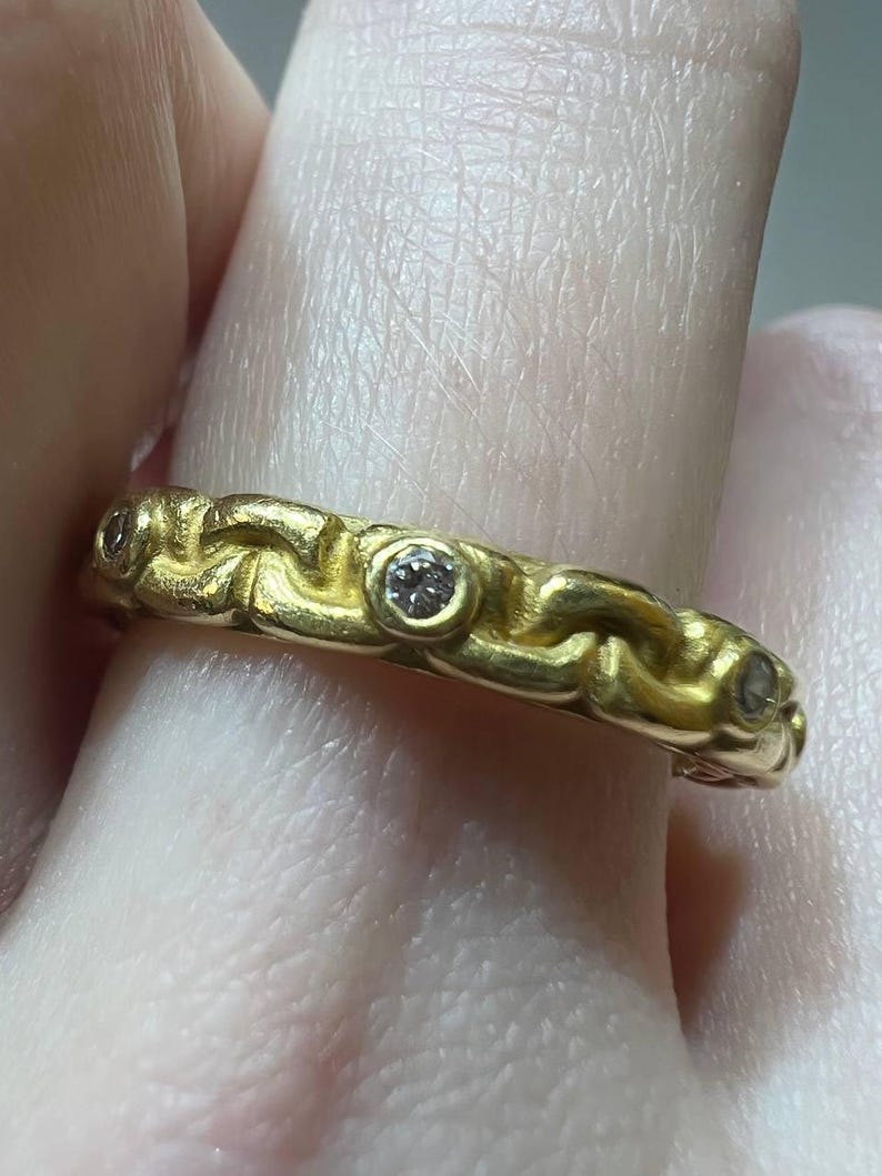 Puede incluir: Un anillo de oro con un dise&ntilde;o texturizado y tejido. El anillo presenta tres peque&ntilde;as piedras preciosas transparentes engastadas en la banda. El anillo es de color oro amarillo c&aacute;lido.
