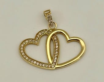 May include: Gold-toned pendant featuring two intertwined hearts. One heart is outlined with small, clear gemstones, while the other is a solid gold. The pendant has a small bail at the top for a chain.