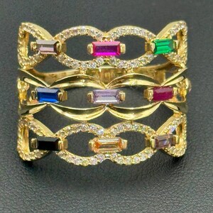 Op de afbeelding: Gouden ring met een meerlaags ontwerp met een reeks kleurrijke rechthoekige edelstenen die in een delicaat, ingewikkeld patroon zijn gezet.