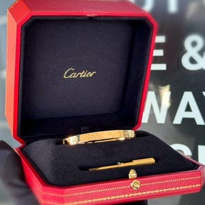 May include: A gold Cartier love bracelet in a red box with the Cartier logo and a small gold screwdriver.