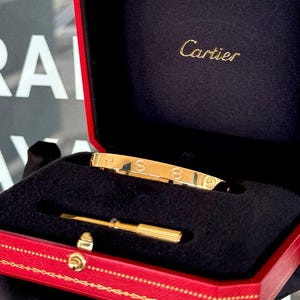 May include: A gold Cartier love bracelet in a red box with the Cartier logo on the lid.