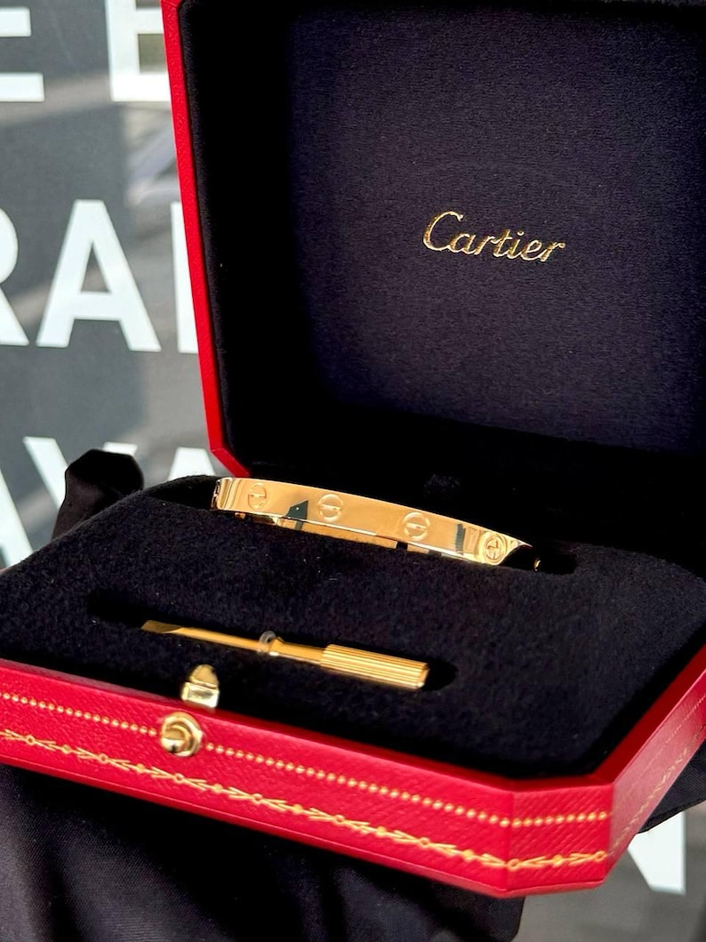 May include: A gold Cartier love bracelet in a red box with the Cartier logo on the lid.