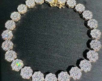 Peut inclure: Un bracelet doré orné d'un motif floral. Chaque fleur est incrustée de nombreuses petites pierres scintillantes. Le bracelet est fermé par un fermoir doré, sur fond sombre.