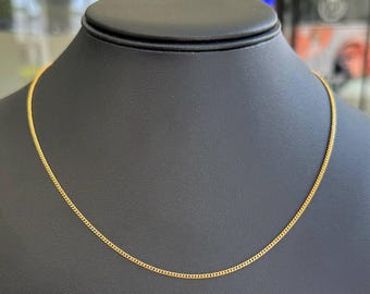 Peut inclure: Un collier chaîne de couleur or présenté sur un mannequin noir. La chaîne présente un design délicat à maillons gourmette. Le collier est présenté sur un fond neutre, soulignant son élégance simple. La chaîne mesure environ 45 cm de long.