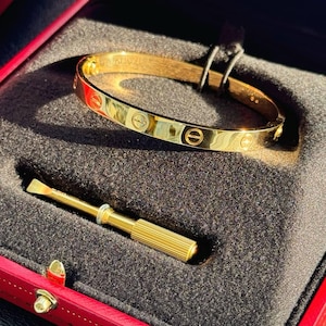 May include: A gold-colored Cartier Love bracelet with a screwdriver in a red velvet box.