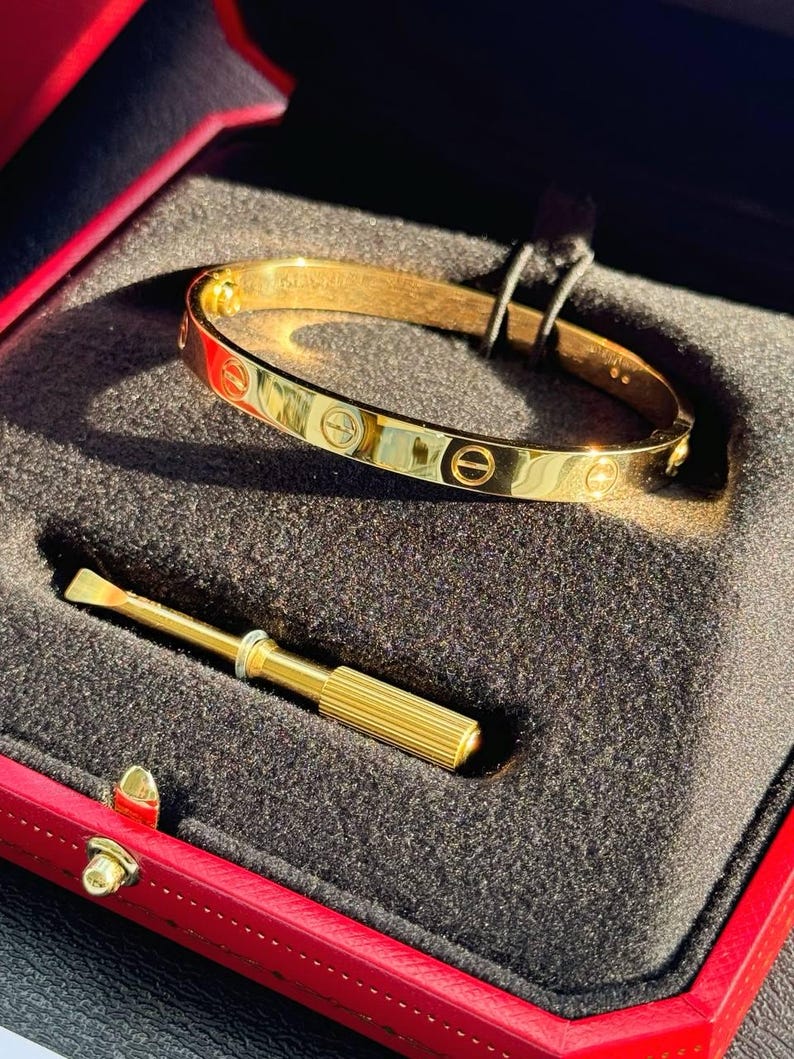 May include: A gold-colored Cartier Love bracelet with a screwdriver in a red velvet box.