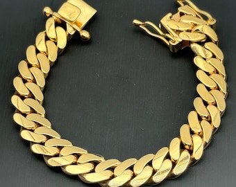 Peut inclure: Un bracelet chaîne gourmette de couleur or avec un fermoir sécurisé. Le bracelet présente une série de maillons arrondis et imbriqués. Le fermoir est rectangulaire et solidement fixé. Le bracelet est présenté sur un fond sombre.
