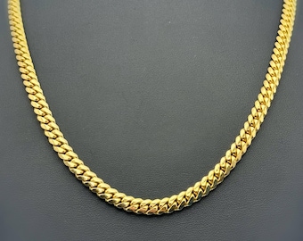 Peut inclure: Un collier chaîne gourmette de couleur or. Le collier est présenté sur un mannequin noir. Les maillons de la chaîne sont épais et étroitement liés, créant un aspect solide et texturé. Le collier est un bijou classique.