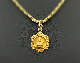 Peut inclure: Un collier pendentif doré avec une figure religieuse détaillée dans un cadre floral. Le pendentif est suspendu à une chaîne délicate et texturée. Le fond est d'une couleur sombre et unie, soulignant le design complexe du collier.