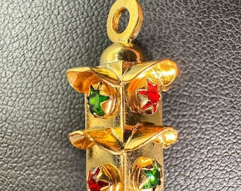 May include: A gold-colored pendant with a geometric design. The pendant features red and green gemstones in a star shape. The pendant has a loop at the top for a chain or cord.