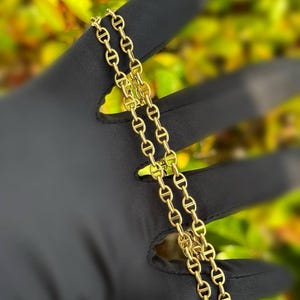 May include: A gold chain necklace with a mariner link design. The chain is folded in half and laid out on a black surface.