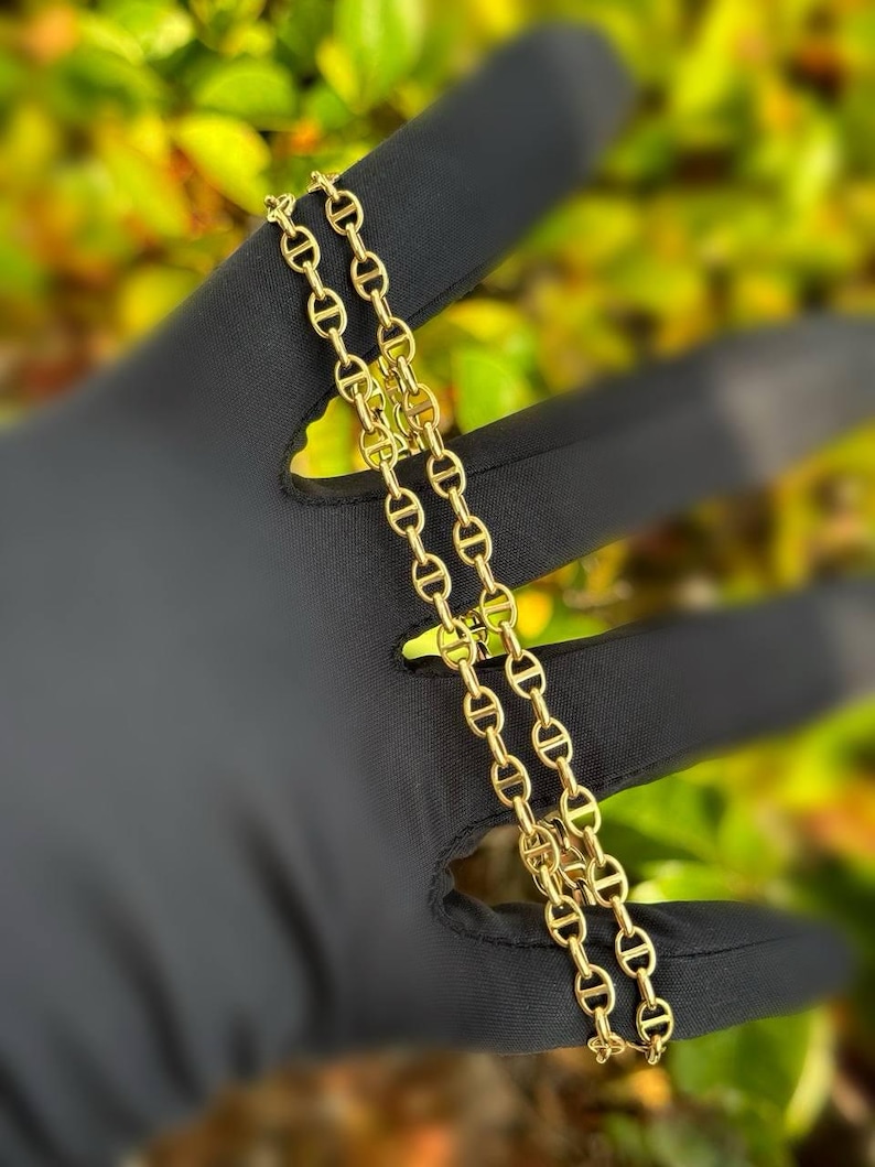 May include: A gold chain necklace with a mariner link design. The chain is folded in half and laid out on a black surface.