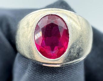 Peut inclure: Une bague en argent avec une grosse pierre précieuse rouge foncé de forme ovale. La pierre est sertie dans un anneau en argent brossé. Le design de la bague est classique et audacieux, adapté au quotidien ou aux occasions spéciales.