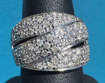 Peut inclure: Une bague en argent avec un design tourbillonnant, incrustée de nombreux petits diamants étincelants. La bague est présentée sur un présentoir noir sur fond bleu, mettant en valeur ses détails et son éclat.