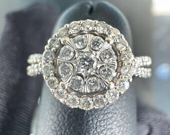 May include: A silver ring with a large round diamond center stone surrounded by smaller diamonds. The ring has a double band.