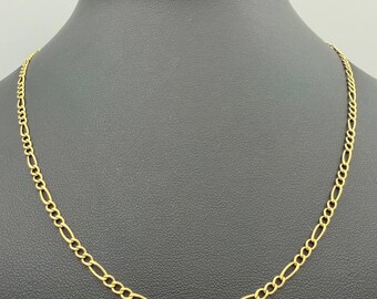 May include: A gold-toned figaro chain necklace featuring a repeating pattern of three small circular links followed by one elongated oval link. The metal chain has a polished finish and is displayed on a dark, rounded neck-shaped jewelry stand.