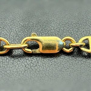 May include: A gold chain necklace with a lobster clasp fastening. The chain is made of oval links with a rope-like design.