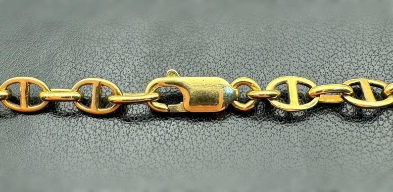 May include: A gold chain necklace with a lobster clasp fastening. The chain is made of oval links with a rope-like design.