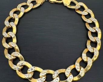 Peut inclure: Un bracelet à maillons de chaîne de couleur or avec un motif texturé sur chaque maillon. Le bracelet est fait d'un matériau métallique brillant et possède un fermoir sécurisé. Le bijou est présenté sur un fond sombre.