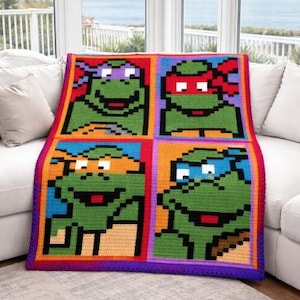 May include: A colorful, handmade crochet blanket featuring four squares with pixelated images of the Teenage Mutant Ninja Turtles. The blanket has a vibrant border and is draped over a white sofa.