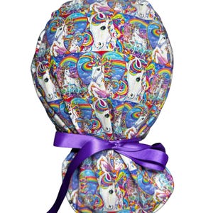 May include: A colorful scrub cap featuring a repeating pattern of white unicorns, rainbows, and hearts on a blue background. The cap is tied with a purple satin ribbon. This item is designed for medical professionals.